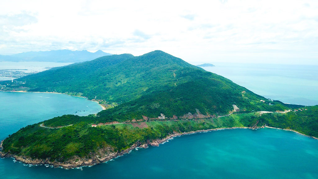 Aerial view of a lush peninsula where tropical forest meets the turquoise sea near Da Nang.