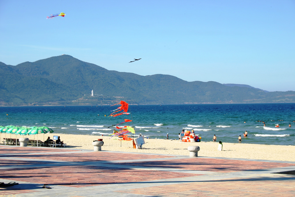 Visitors swimming in calm, crystal-clear coastal waters under a bright blue sky.